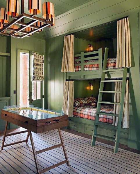 Cozy green bunk beds with plaid bedding, privacy curtains, built-in drawers, and a retro foosball table for a fun kids' room
