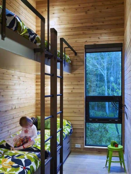 Modern bunk beds in a wood-paneled room with vibrant green bedding, large windows, and a cozy reading corner for kids