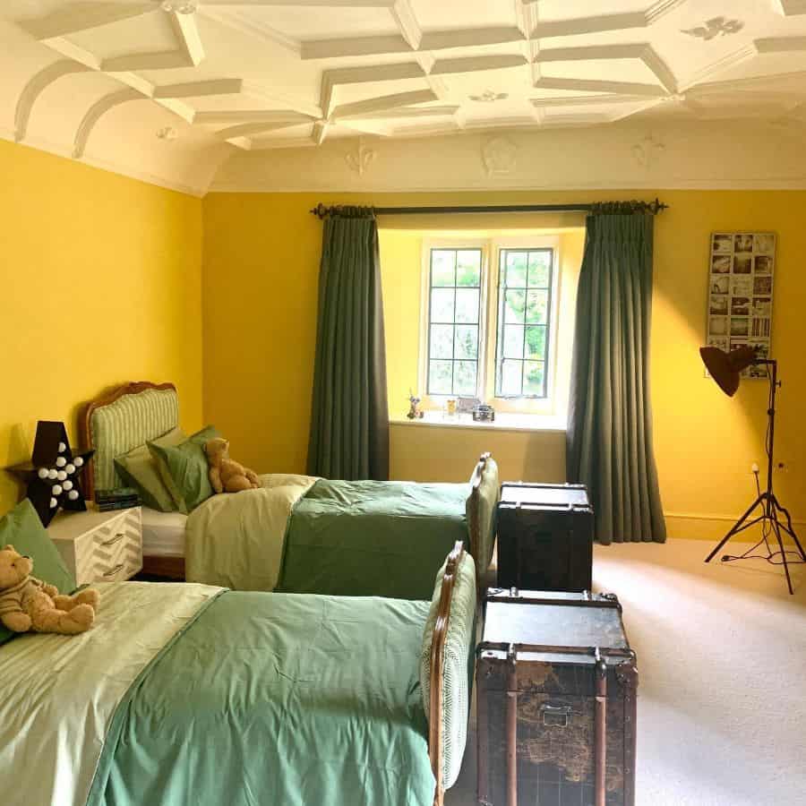 A cozy bedroom with twin beds, green bedding, yellow walls, and a window adorned with yellow curtains