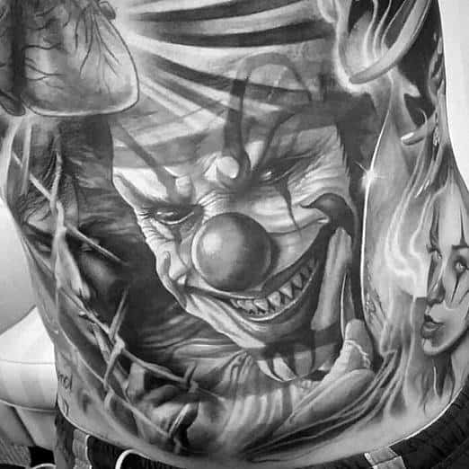 Black and grey tattoo of a sinister clown with a menacing grin, bold shading, and eerie details for a haunting and intense horror design.
