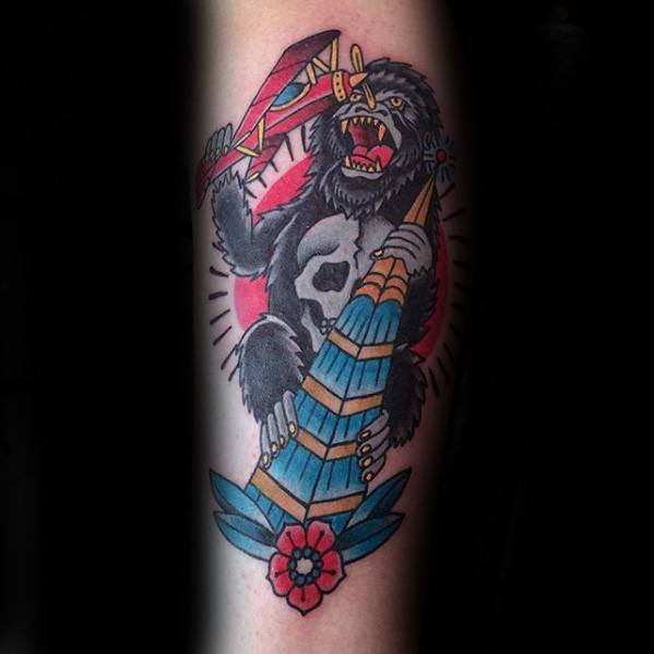 Traditional King Kong tattoo with bold colors, showing Kong climbing a tower while swatting a red biplane, framed by a red sunburst.
