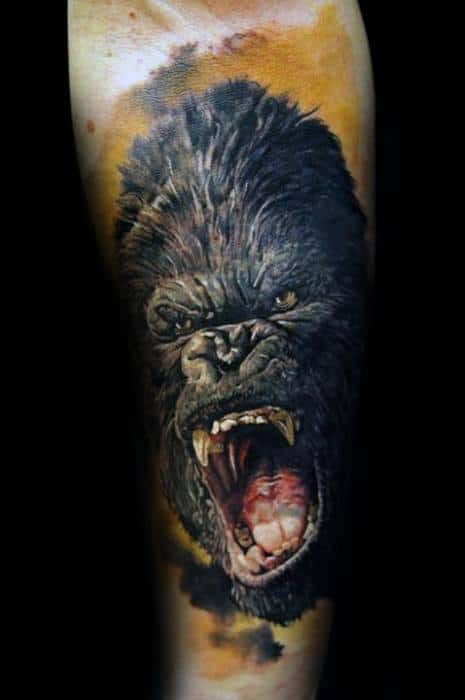 Realistic King Kong tattoo with intense expression and open mouth, set against a dramatic orange and black cloudy sky background.