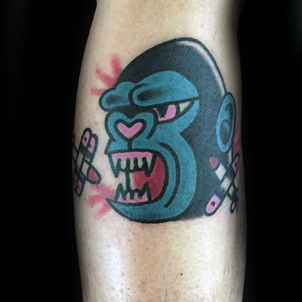 Cartoon-style King Kong tattoo with teal and pink tones, featuring a fierce expression, heart-shaped nose, and bandages on both sides.