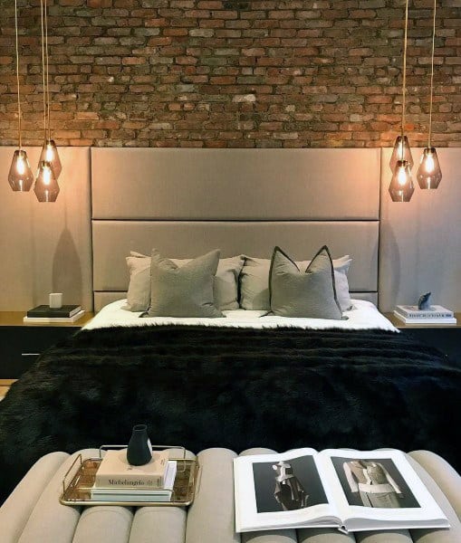 Modern bedroom with exposed brick wall, pendant lighting, and plush bedding.