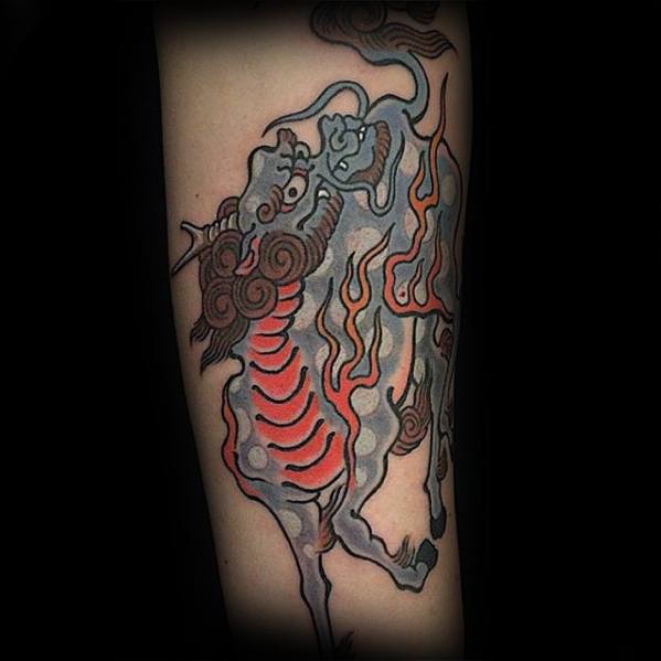 Stylized Kirin tattoo with muted blue-grey tones, red belly scales, and orange flames, drawn in a bold, illustrative traditional style.