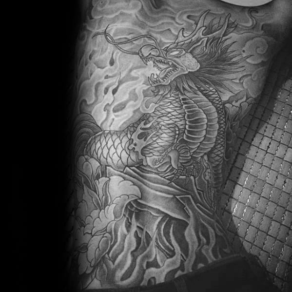 Black and grey Kirin tattoo on the side torso, with bold flames, sharp scales, and intense detail flowing from the hip to the ribs.