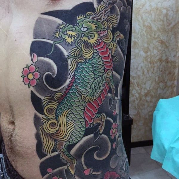 Side torso Kirin tattoo with green scales, golden mane, and red chest, surrounded by black clouds and pink cherry blossoms.