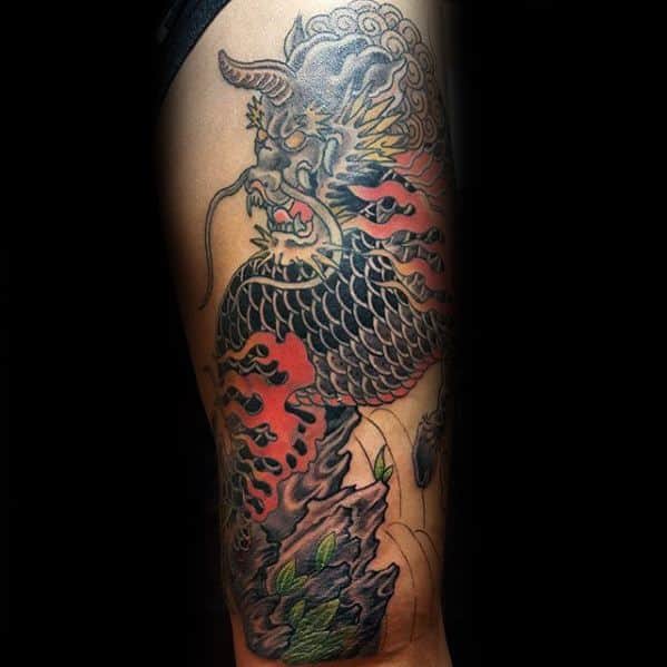 Kirin tattoo on the thigh with black scales, red flames, and golden details, set against rocks and leaves in a bold traditional style.