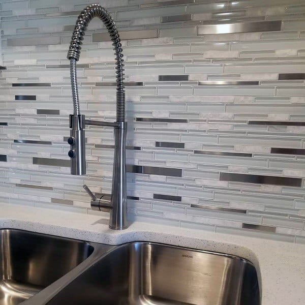 Sleek glass and metal mosaic tiles complement the stainless steel faucet and sink for a modern, polished kitchen look.