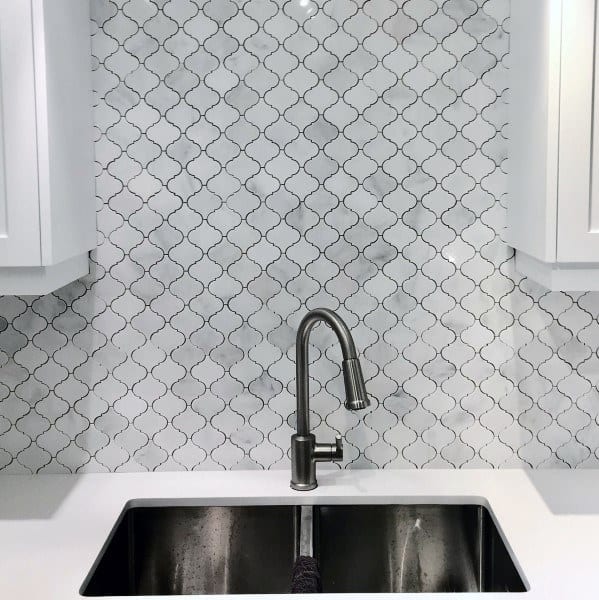 Stainless steel sink with arabesque tile backsplash and white cabinets.
