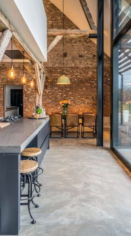Industrial kitchen with exposed brick walls, wooden beams, and modern bar stools.
