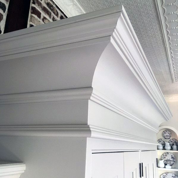A close-up of white kitchen cabinetry with decorative crown molding, blending beautifully with the ceiling and vintage-style plates on display