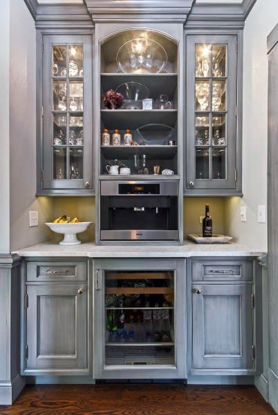 Elegant coffee bar with grey cabinets, glass display doors, built-in coffee machine, and beverage cooler.