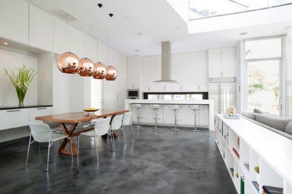 Modern kitchen with copper pendant lights, concrete floors, a wooden table with white chairs, and a breakfast bar