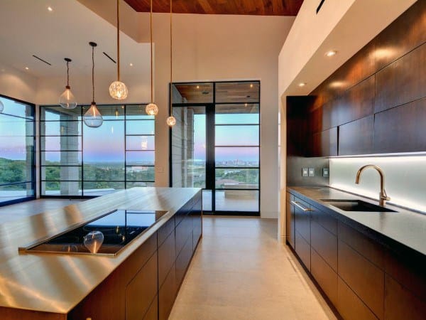 Modern kitchen with wooden cabinets, island cooktop, island pendant lights, and large windows showcasing the outdoor view