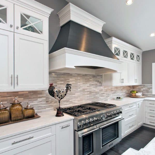 Traditional kitchen with white cabinets, a neutral stone backsplash, a bold black range hood, and stainless steel appliances