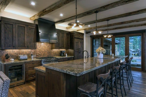 Dark rustic kitchen with wood-beamed ceiling, large granite countertop island, and pendant lighting.