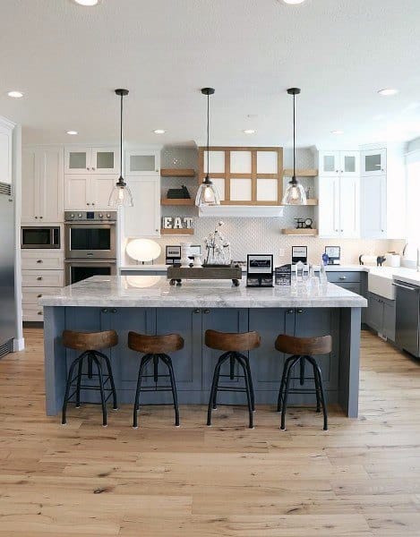 Rustic kitchen with blue island, marble countertop, pendant lights, and white cabinets.