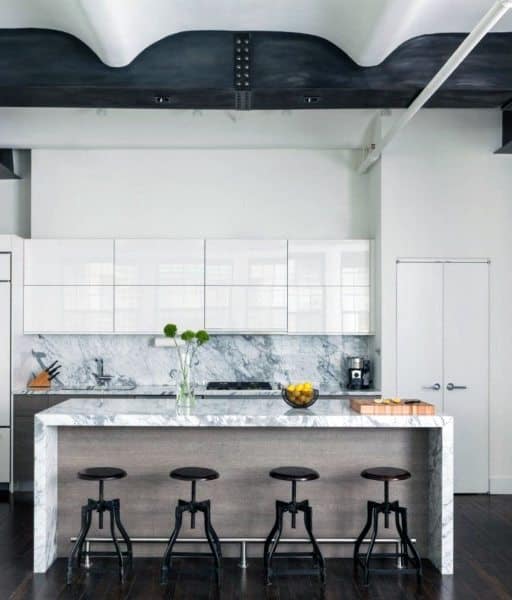 Modern industrial kitchen with a white marble island, sleek cabinets, and black barstools on dark hardwood flooring.