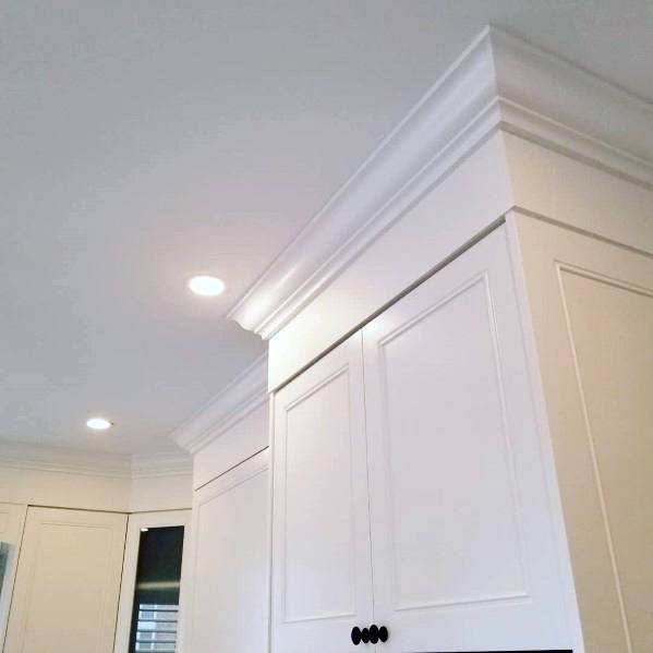A kitchen corner featuring white cabinetry with simple, clean crown molding, recessed lighting, and sleek black hardware for a minimalist design