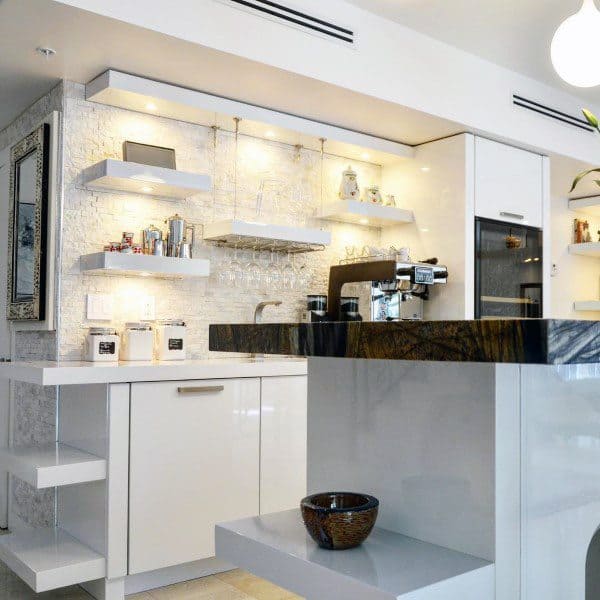 Sleek coffee bar with white cabinets, floating shelves, backsplash lighting, and espresso machine.