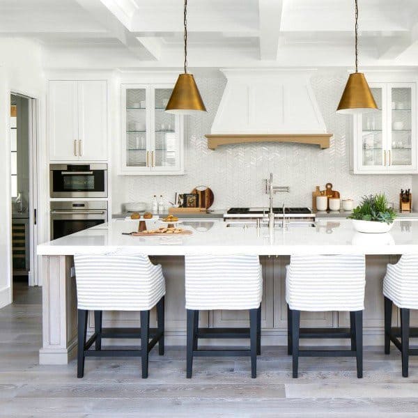 Modern kitchen with a spacious island, white cabinets, striped bar stools, and pendant lights