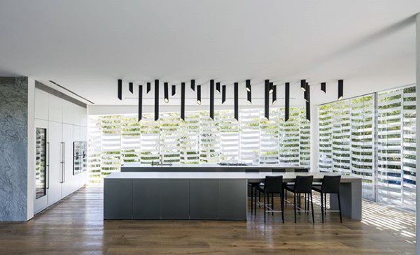 Modern kitchen with a spacious island, sleek black chairs, and unique ceiling lights; glass walls with striped shades