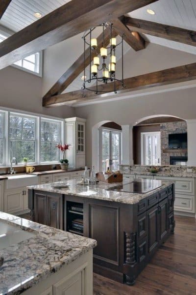 Elegant kitchen with exposed beams, a spacious marble island, and a chandelier under a high ceiling