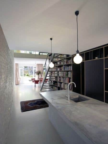 Minimalist loft kitchen with concrete island, library wall, and modern pendant lighting.