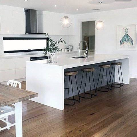 Minimalist kitchen with white island, wood barstools, hardwood floors, and pendant lighting.