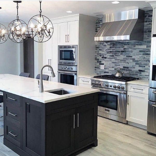 Modern kitchen with dark island, stainless steel appliances, mosaic backsplash, and elegant lighting.