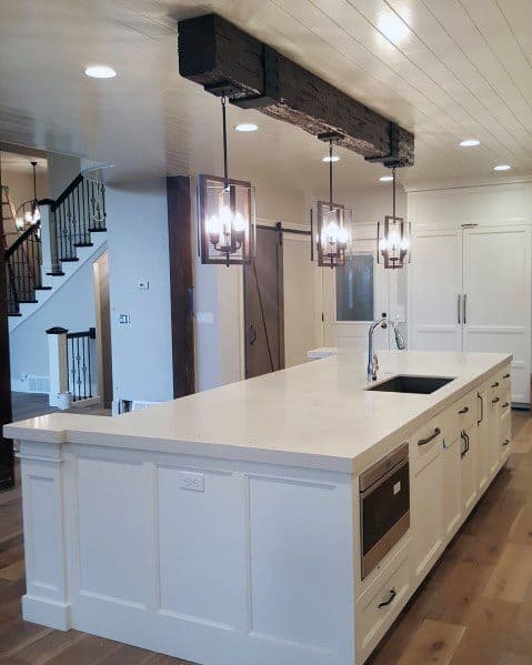Farmhouse kitchen with white shiplap ceiling, exposed wood beam, large island, and pendant lights.