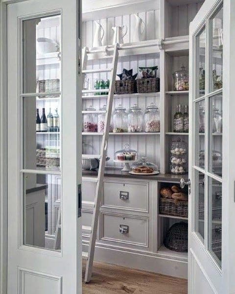 Charming kitchen pantry with glass-paneled doors, a built-in ladder, open shelving, and wicker storage baskets.