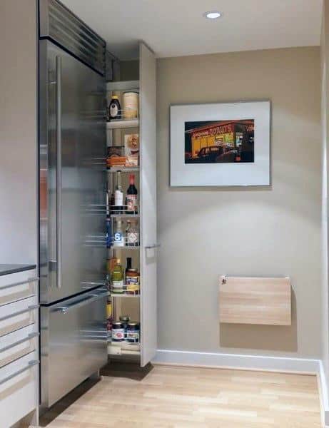 Slim pull-out pantry beside a stainless steel refrigerator in a modern kitchen.