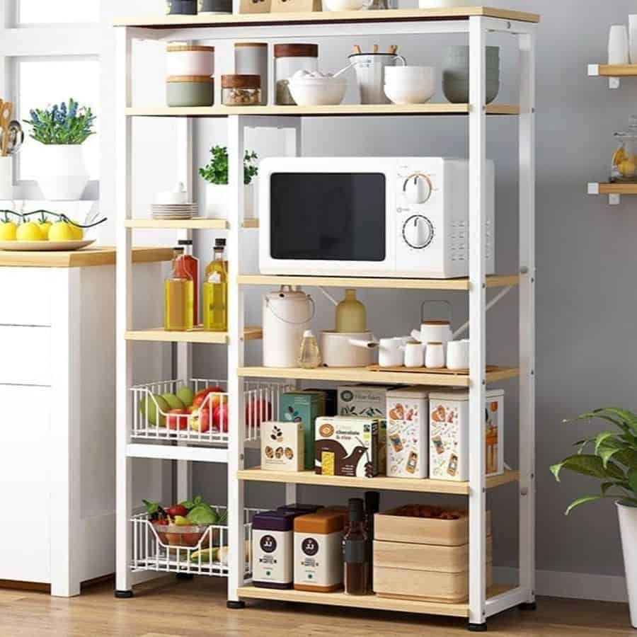 Kitchen storage rack with shelves holding microwave jars fruits and pantry essentials.