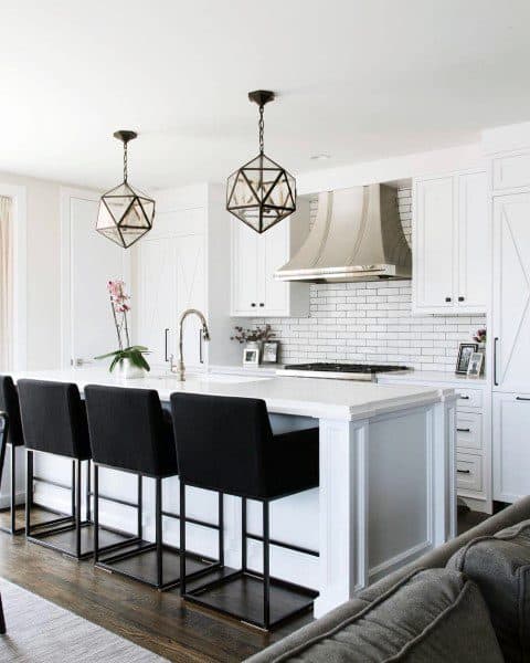 White kitchen with geometric pendant lights black barstools and subway tile backsplash.