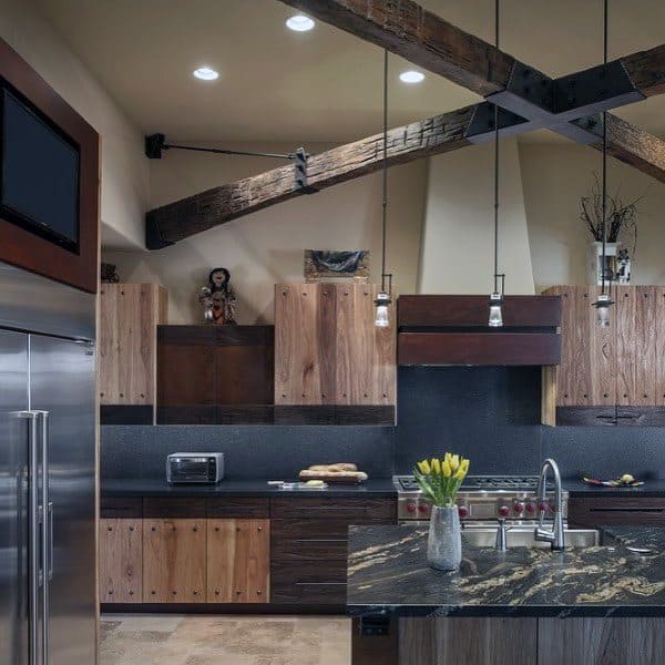 Rustic kitchen with exposed wooden beams, dark countertops, wood cabinets, and pendant lighting.