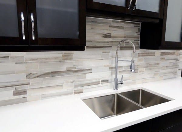 Glass tile backsplash with earthy tones complements the sink and dark cabinets.