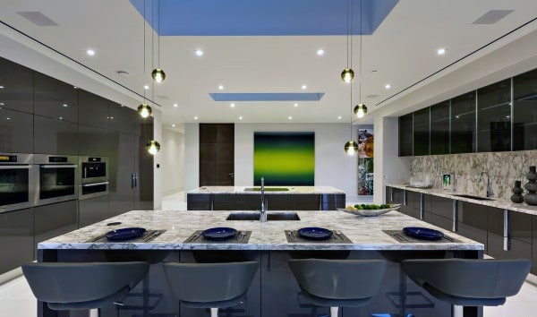 Modern kitchen with marble countertops, gray cabinets, island, pendant lights, and a green abstract painting on the wall