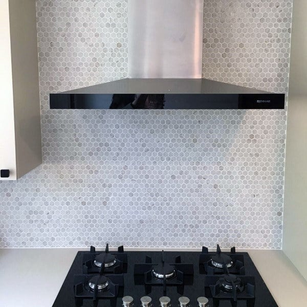 White hexagon tile backsplash with black stovetop and stainless steel range hood.
