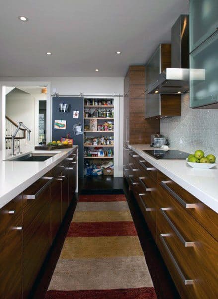 Sleek kitchen with wooden cabinets, white countertops, and a walk-in pantry at the end.