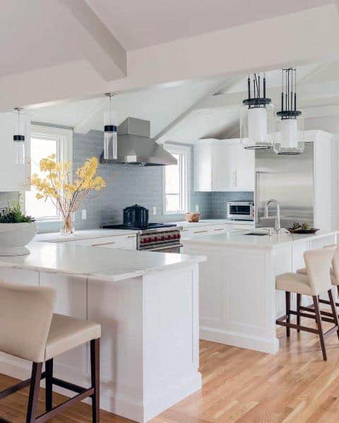 White kitchen with vaulted ceiling, grey backsplash, pendant lighting, and modern seating.