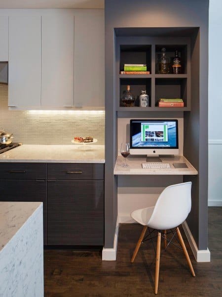 Compact home office nook with a built-in desk, white chair, and shelves nestled between modern kitchen cabinets