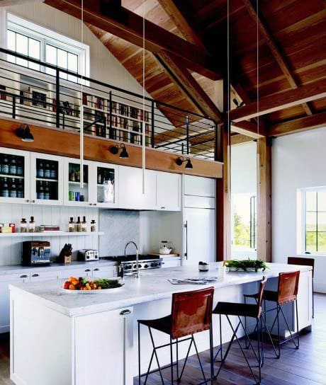 Modern kitchen with marble countertops, high ceilings, and a loft library above.