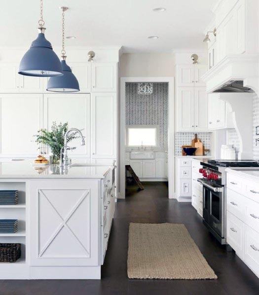 White kitchen with blue pendant lights, large island, and dark hardwood floors.