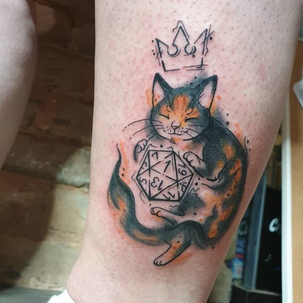 Artistic tattoo of a calico cat holding a D20 dice, with a Kingdom Hearts crown above its head, blending watercolor and fine line styles.