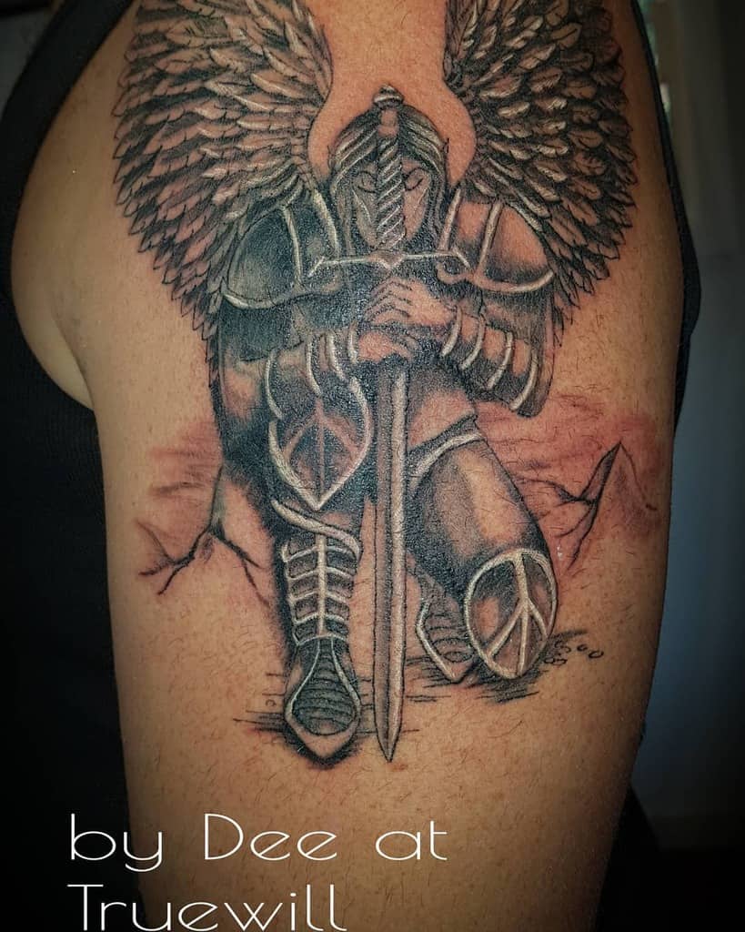 Black and white tattoo of a winged warrior angel knight kneeling with a sword on a rocky field