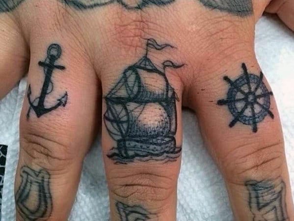Nautical-themed finger tattoos featuring an anchor, sailing ship, and ship wheel, symbolizing adventure, stability, and a deep connection to the sea.