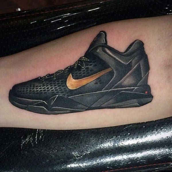 A detailed tattoo of a black and gold Kobe Bryant Nike shoe, showcasing realistic shading and design.