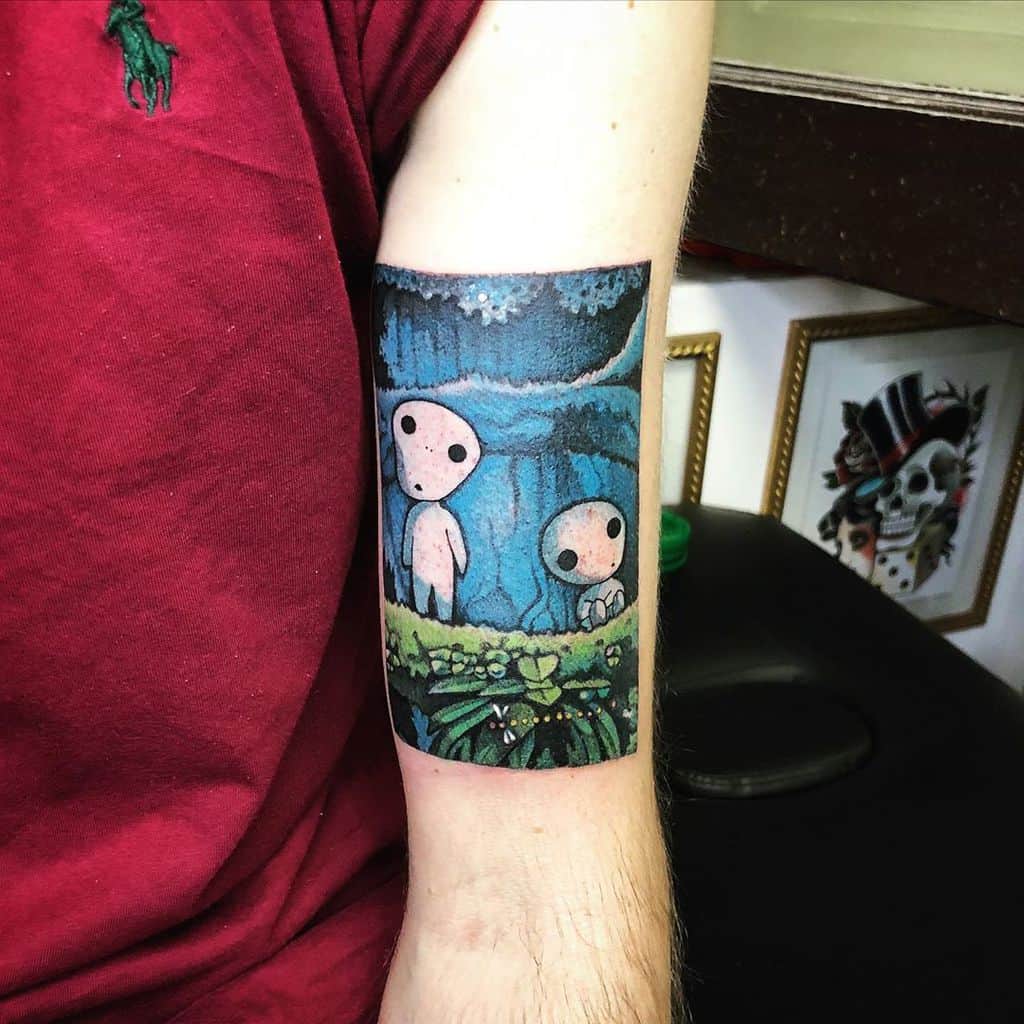 Forearm tattoo of kodama spirits in a mystical forest scene, inspired by Princess Mononoke, with glowing moonlight and lush greenery.